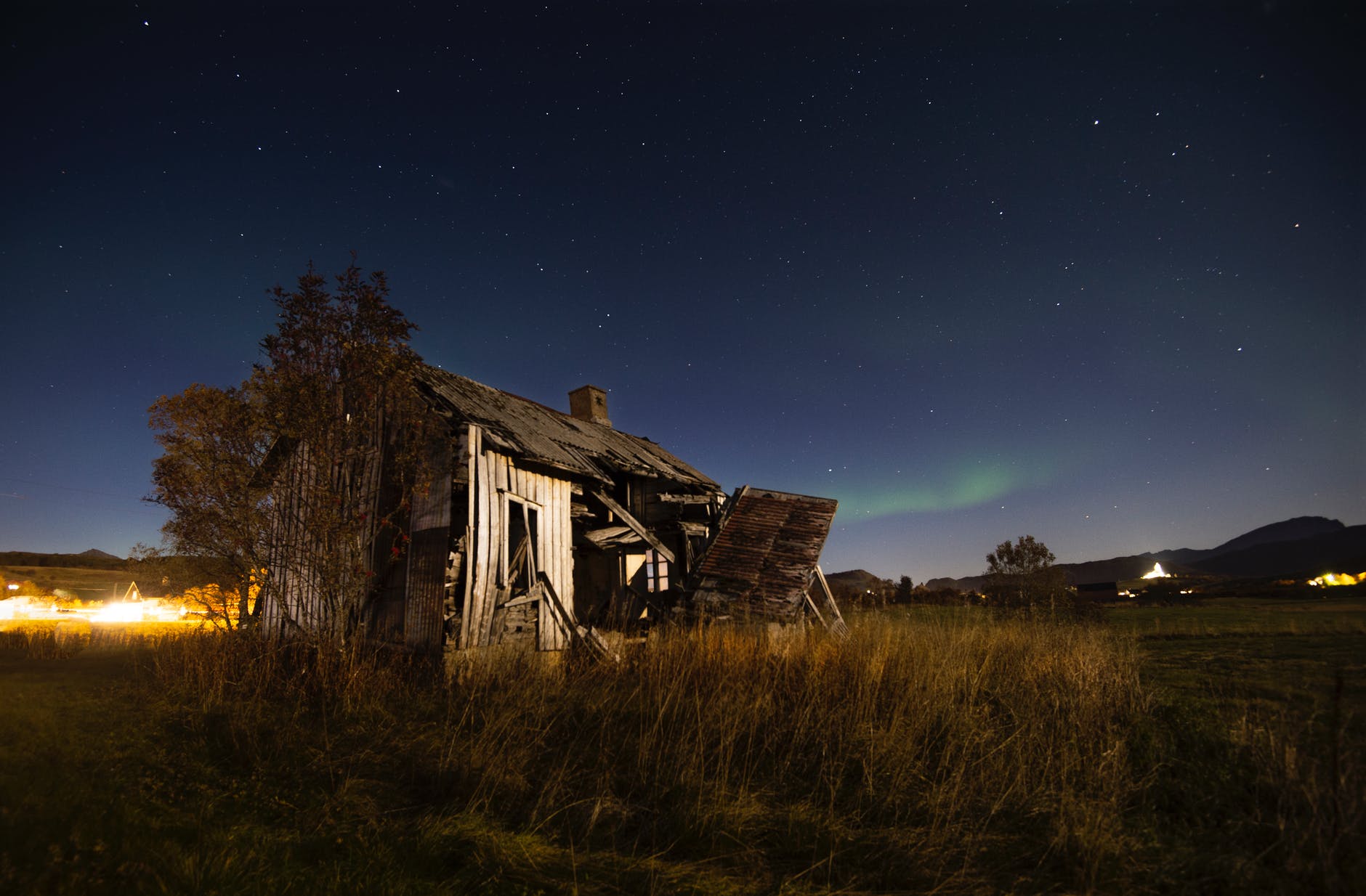abandoned wooden barn on grassy terrain against starry night sky
